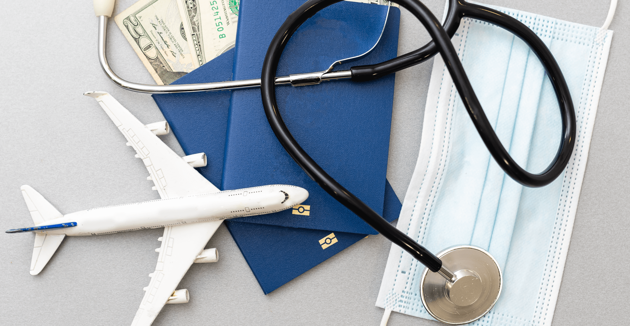 Travel and healthcare concept. Top view of face mask, hand sanitizer, passport, stethoscope and toy plane isolated on blue background with copy space.