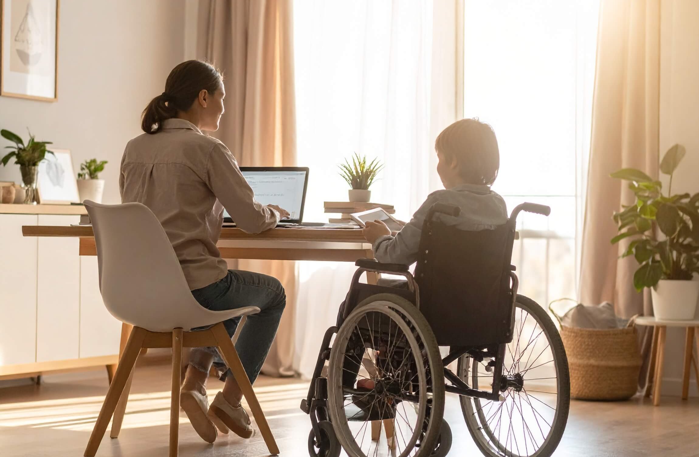 A-home-office-scene-viewed-from-behind-a-mother-sitting-at-a-desk-working-on-a-laptop